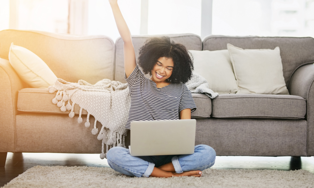 A woman of color relaxing at home with a laptop in her lap and one arm stretching.
