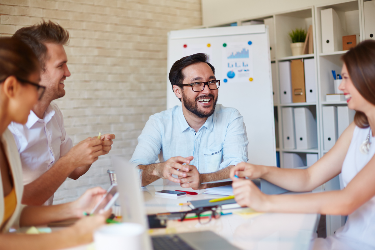 Photo of four smiling employees in a brainstorming session; happy employees create a loyal employee culture.