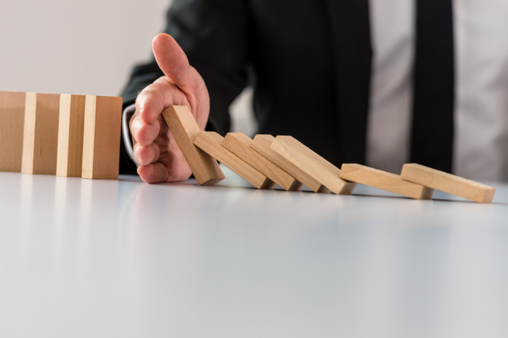 Hr And Management: Coping With Corporate Crisis 2 A business person holding their hand out to stop a domino effect.