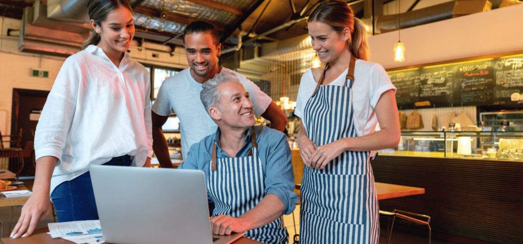 Restaurant workers in aprons gathered around a laptop.