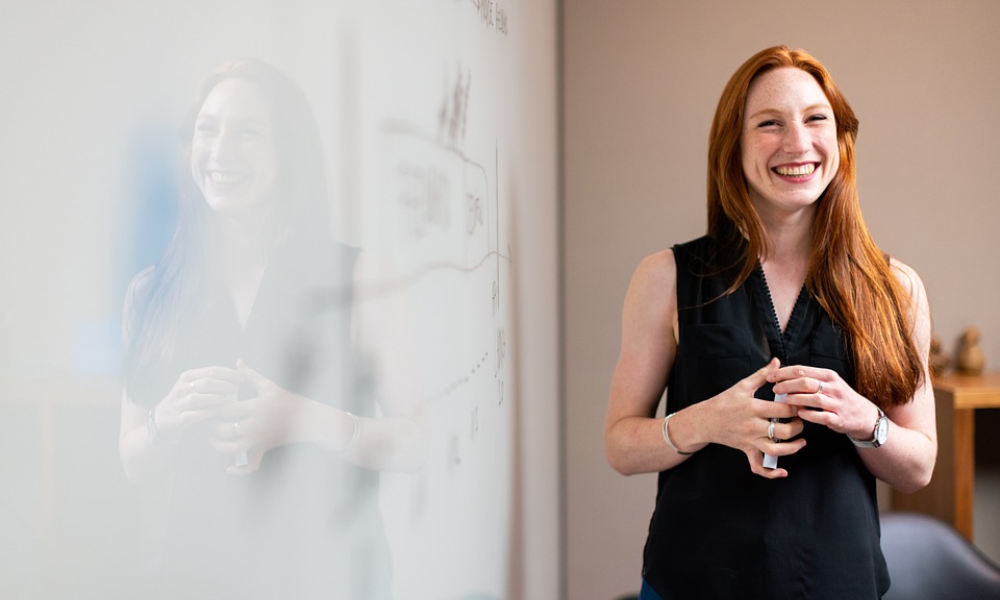 Communication Soft Skills You Need At Work And How To Use Them 3 Female employee smiling beside a whiteboard