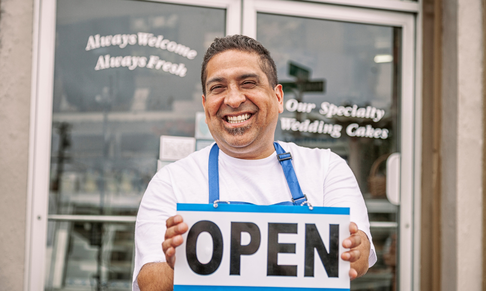Smiling bakery owner holding OPEN sign.