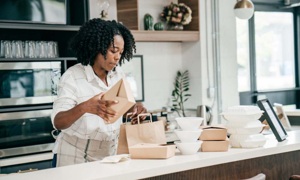 Woman in apron packing to go containers.