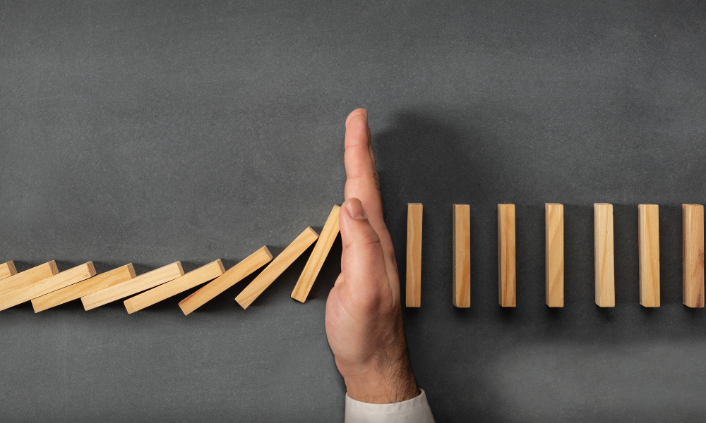 Hand stopping a line of blocks from the domino effect.