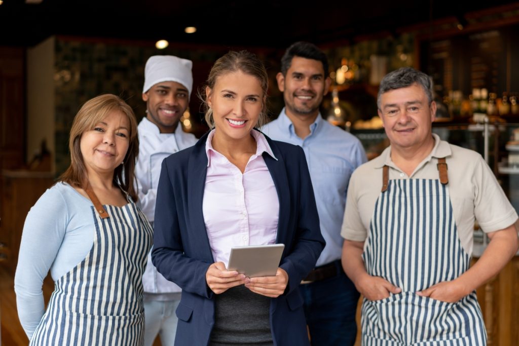 Smiling restaurant manager standing with a diverse team of chefs and staff members wearing aprons inside a restaurant
