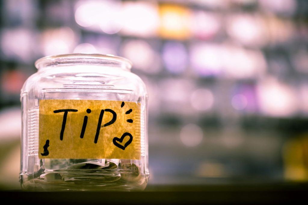 Close-up of a glass tip jar labeled “Tip” with a heart symbol, representing restaurant employees affected by the No tax on tips 2025–2026 rule.